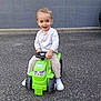 Naël participe au concours pour gagner de l'argent avec cette photo : child, toddler, toy, tractor, green, outdoor, pavement, smiling, happy, boy, white_shoes, striped_shirt, play, fun, vehicle, small, cute, casual_clothing, young, person