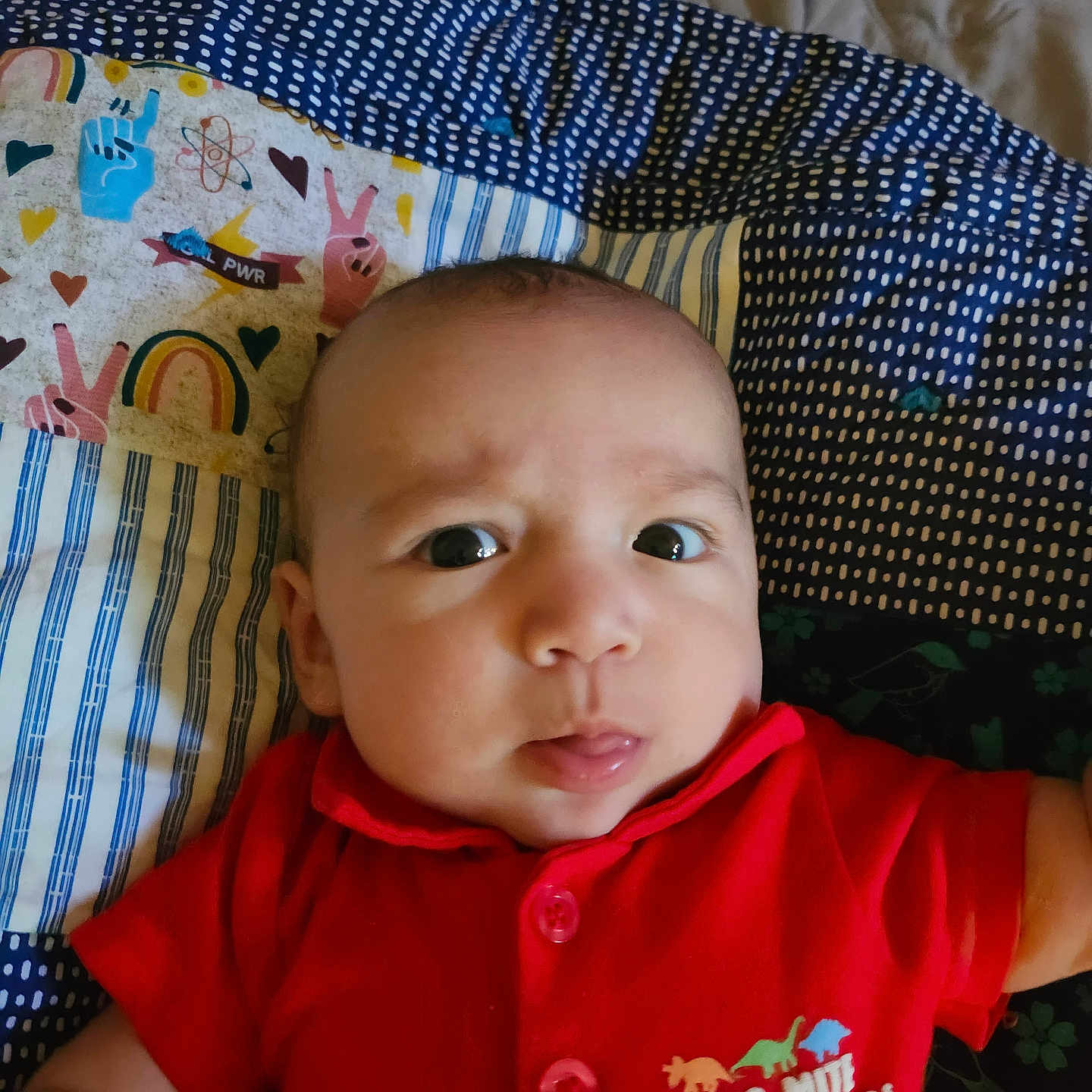 Amiri Lion joined the competition — help win amazing prizes! apparel, baby, blanket, child, closeup, curious_expression, cute, dinosaur_print, face, indoors, infant, lying_down, patterned_blanket, peace_sign, person, portrait, rainbow, red_shirt, tongue_out, young