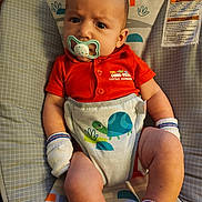 Amiri Lion joined the competition — help win amazing prizes! baby, infant, pacifier, orange_onesie, mittens, socks, baby_seat, turtle_pattern, monkey_pattern, face, expression, child, cute, indoors, comfortable, clothing, newborn, portrait, resting, baby_girl