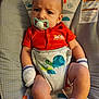 baby, infant, pacifier, orange_onesie, mittens, socks, baby_seat, turtle_pattern, monkey_pattern, face, expression, child, cute, indoors, comfortable, clothing, newborn, portrait, resting, baby_girl