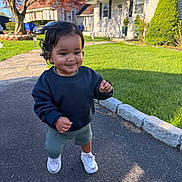 Noah joined the competition — help win amazing prizes! toddler, child, curly_hair, sneakers, sweatshirt, shorts, sidewalk, driveway, grass, tree, house, daylight, smiling, outdoor, suburban, person, young_child, walking, shadow, nature