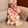 armchair, baby, bow, child, clothing, cozy, cute, face, happy, headband, indoors, infant, patterned_fabric, person, pink_clothing, portrait, sitting, smiling, soft_lighting, young_child