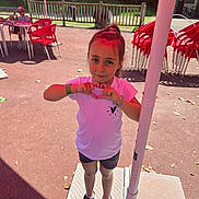 Myléna participe au concours pour gagner de l'argent avec cette photo : child, girl, outdoor, sunny, heart_shape, white_shirt, black_shorts, sneakers, red_chairs, table, umbrella, fence, bracelet, hair_tie, pavement, playground, daylight, person, casual_wear, smiling