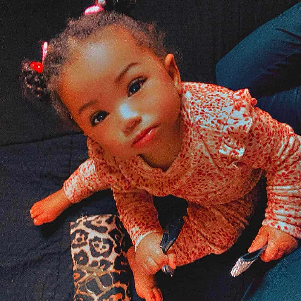 Paris is registered to the contest to win money with this photo: toddler, child, pigtails, curious, indoor, leopard_print, pouch, black_surface, clothing, patterned_outfit, person, cute, looking_up, baby, hands, foot, sitting, bright_eyes, hair_ties, young_child