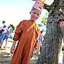blurred_background, bracelet, brown_clothing, celebration, child, costume, crown, daytime, festival, fox, grass, hand, happy, nature, outdoor, people, portrait, smile, sunlight, tree
