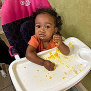 Autumn joined the competition — help win amazing prizes! toddler, high_chair, food, scrambled_eggs, messy, child, curly_hair, pink, orange_shirt, indoor, tray, eating, face, hands, floor, tile_floor, wall, person, baby_food, expression
