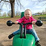 bench, child, daylight, fun, green_toy, grip, happy, jeans, outdoor, park, person, pink_jacket, play_equipment, playground, puma, smiling, sneakers, toddler, toy_vehicle, tree