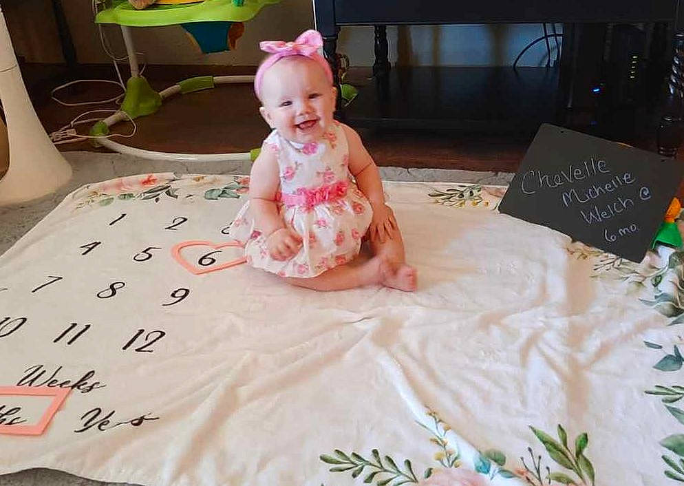 Chevelle is registered to the contest to win money with this photo: baby, baby_toddler_clothing, bed_sheet, bedding, birthday, child, dress, event, flooring, fun, green, happy, joy, leisure, linens, person, pink, room, sitting, smile