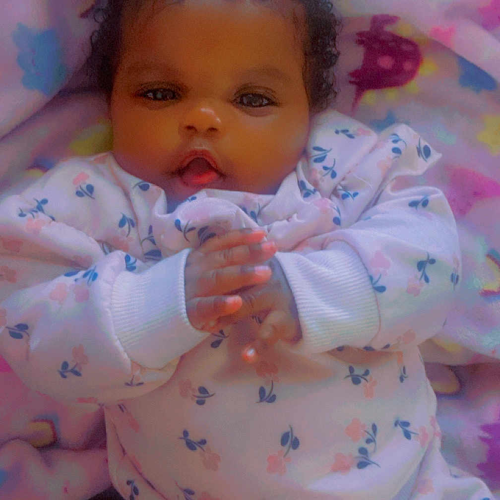 Deasia is registered to the contest to win money with this photo: baby, blanket, blue, child, clothing, curly_hair, cute, eyes, face, floral_outfit, hands, indoor, infant, lying_down, pink, portrait, soft_lighting, star_pattern, warm, yellow