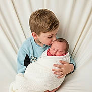 Kenza participe au concours pour gagner de l'argent avec cette photo : child, baby, newborn, swaddled, kiss, affection, brother, family, portrait, soft_background, blanket, cute, love, tenderness, caucasian, sitting, indoor, cozy, gentle, peaceful