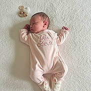 Kenza a rejoint le concours — aidez-le/la à gagner de superbes lots ! adorable, baby, bunny_slippers, child, cozy, cute, indoors, infant, knitted_heart, lying_down, newborn, peaceful, pink_onesie, portrait, resting, sleeping, small_toys, soft_texture, white_blanket, wooden_toy