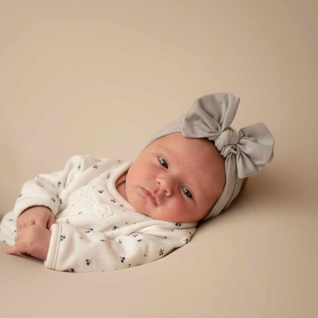 Kenza a rejoint le concours — aidez-le/la à gagner de superbes lots ! baby, bow, child, clothing, cute, expression, face, headband, indoors, infant, lying_down, minimalistic, neutral_background, newborn, peaceful, portrait, resting, skin, small_hands, soft_lighting