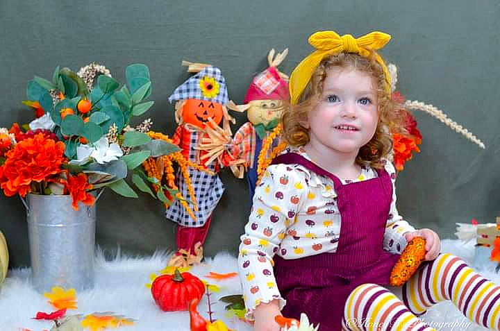Lillian is registered to the contest to win money with this photo: annual_plant, baby_toddler_clothing, calabaza, child, event, floral_design, flower, flower_arranging, flowerpot, fun, happy, houseplant, joy, orange, person, plant, pumpkin, smile, sock, spring