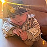baby, child, hat, cap, plaid_jacket, cozy, sunlight, window, leather_chair, indoor, warm_light, smiling, cute, person, seated, young_child, fashion, portrait, casual, comfortable