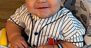 Mateo joined the competition — help win amazing prizes! baby, baseball_jersey, child, cute, face, furniture, hand, happy, home, indoor, infant, person, seat, smiling, stairs, striped_shirt, toy, walker, watch, wood_floor