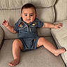 Jesse is registered to the contest to win money with this photo: baby, child, infant, couch, sofa, blue_clothing, romper, cartoon_characters, relaxed, smiling, indoors, furniture, cute, chubby_cheeks, happy, person, sitting, barefoot, short_hair, skin
