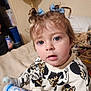 toddler, child, blue_eyes, curly_hair, bows, sweater, mickey_mouse, leopard_print, bed, blanket, bottle, indoor, person, casual, home, cozy, face, expression, curious, soft_lighting
