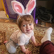 Divinity is registered to the contest to win money with this photo: toddler, bunny_ears, child, crawling, carpet, indoor, playful, smiling, baby_gate, blanket, foot, sock, pants, person, headband, pink, white, brown_hair, striped_shirt, gray_pants