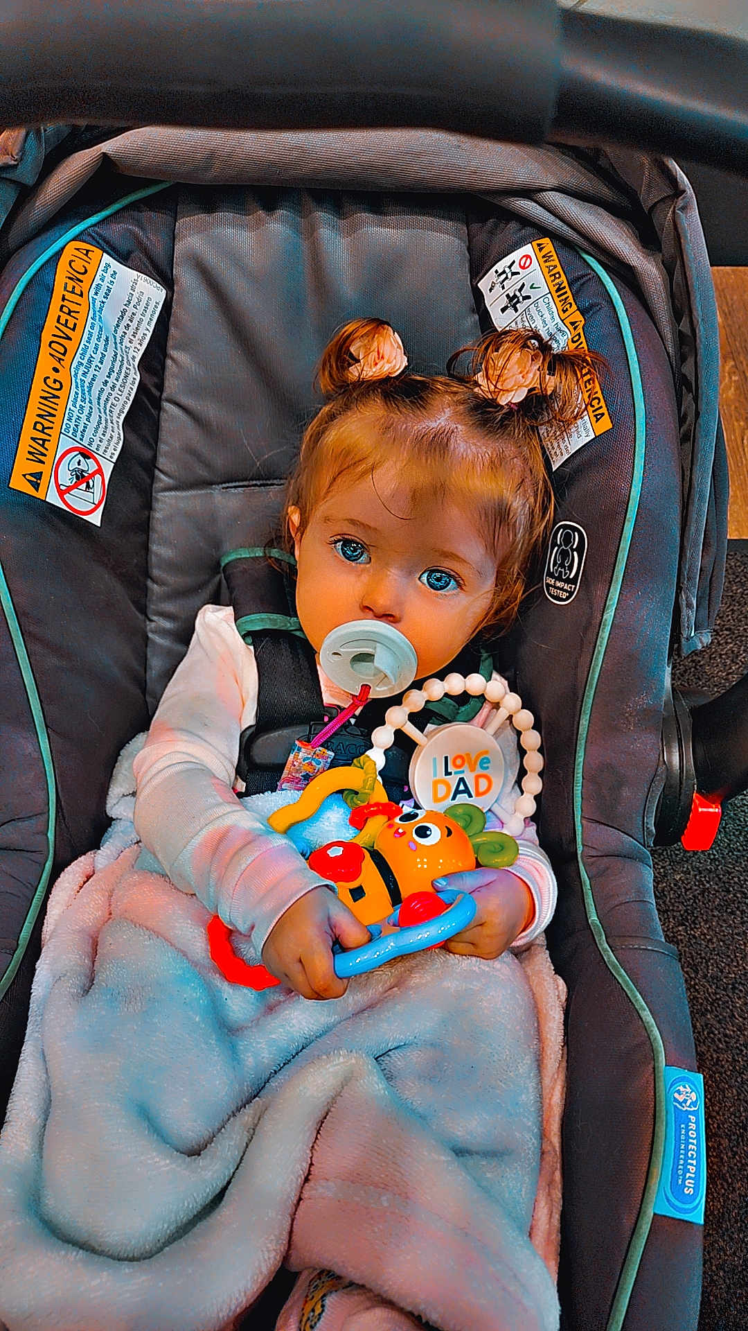 Divinity joined the competition — help win amazing prizes! toddler, child, car_seat, pacifier, toy, blanket, hair_buns, blue_eyes, indoor, cute, infant, baby, clothing, sitting, holding, colorful_toy, warm, comfort, person, portrait