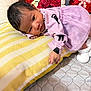 baby, infant, pillow, purple_dress, black_cat_print, lying_down, curious_expression, cushion, yellow_stripes, blanket, indoor, soft_lighting, newborn, cute, cozy, person, face, hand, footwear, home