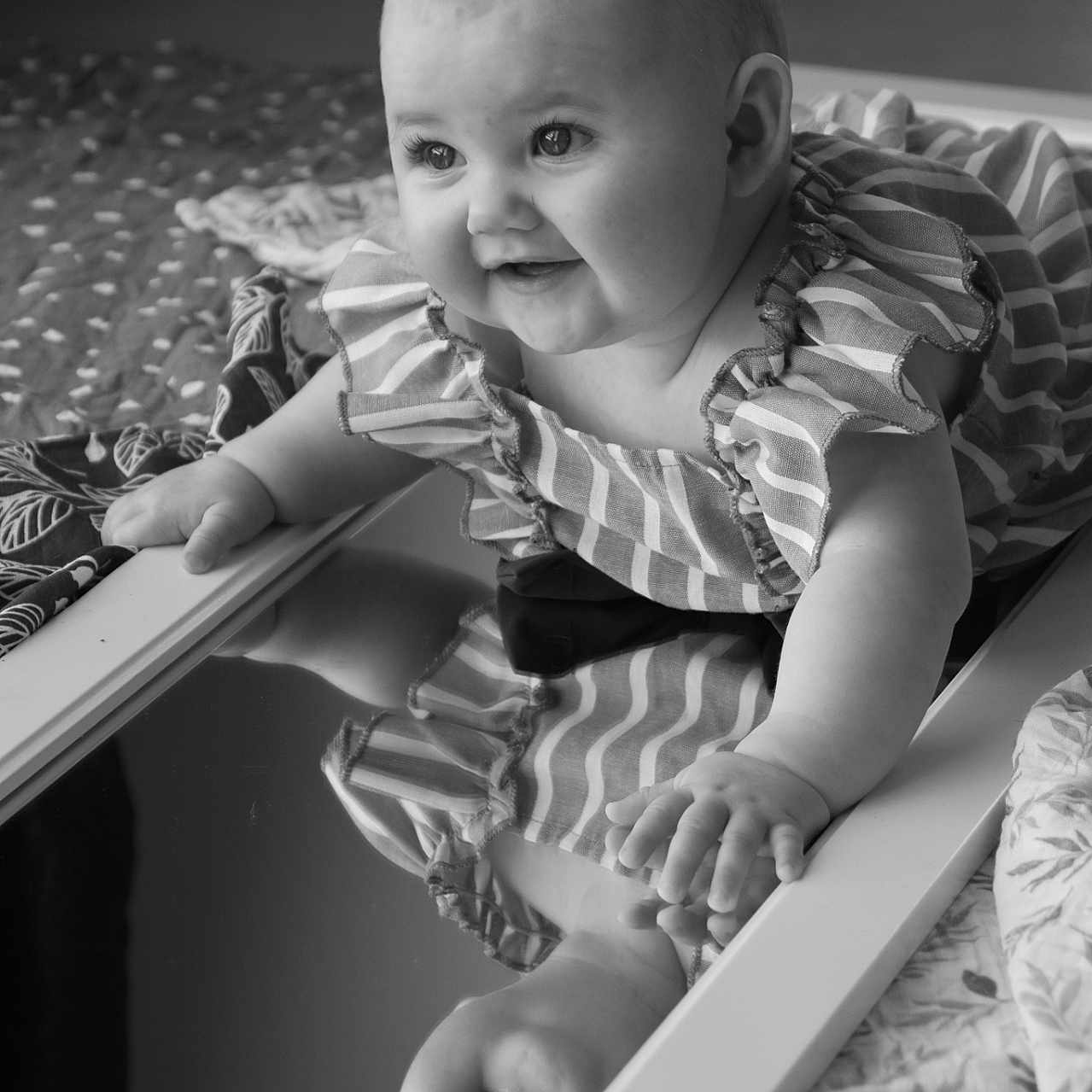 Mia participe au concours pour gagner de l'argent avec cette photo : baby, bedspread, black_and_white, child, closeup, curly_hair, cute, expression, face, hand, happy, indoor, infant, mirror, person, portrait, reflection, smile, striped_clothing, texture