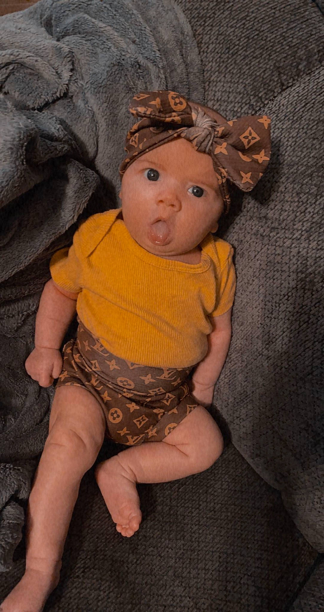 Paisley Rose is registered to the contest to win money with this photo: abdomen, baby, baby_toddler_clothing, cheek, eye, fawn, foot, grass, head, headgear, headwear, human_leg, knee, leg, person, sitting, skin, sleeve, surprise, thigh