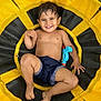 toddler, child, smiling, shirtless, shorts, toy, water_gun, swing, yellow, black, grass, outdoor, play, happy, barefoot, dirt, fun, summer, face, person