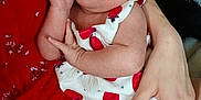 Zayla is registered to the contest to win money with this photo: baby, infant, child, person, hand, arm, red_dress, white_outfit, strawberry_pattern, cute, portrait, indoor, skin, face, eyes, baby_clothes, holding, adult_hand, close_up, expression