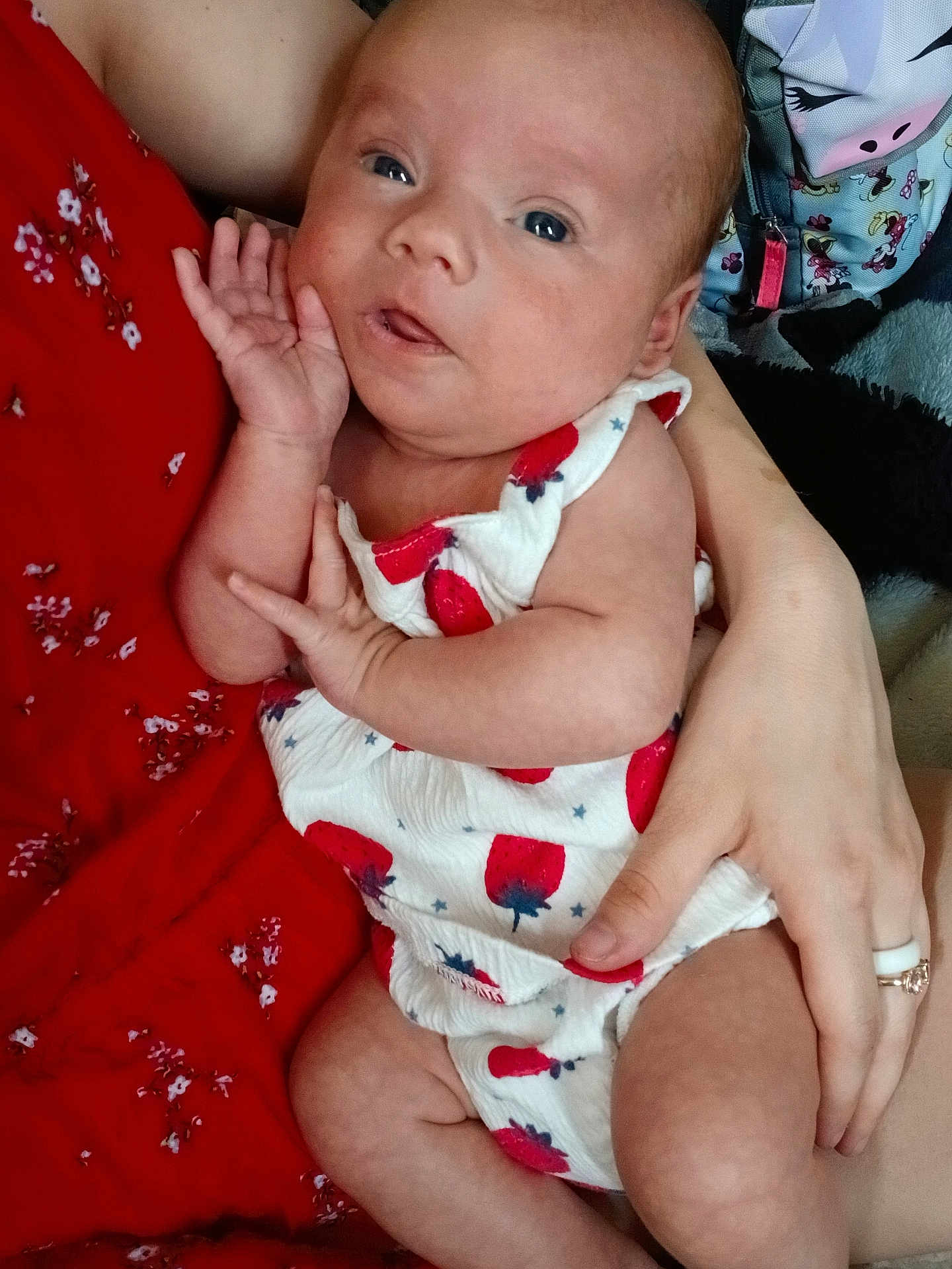Zayla is registered to the contest to win money with this photo: baby, infant, child, person, hand, arm, red_dress, white_outfit, strawberry_pattern, cute, portrait, indoor, skin, face, eyes, baby_clothes, holding, adult_hand, close_up, expression