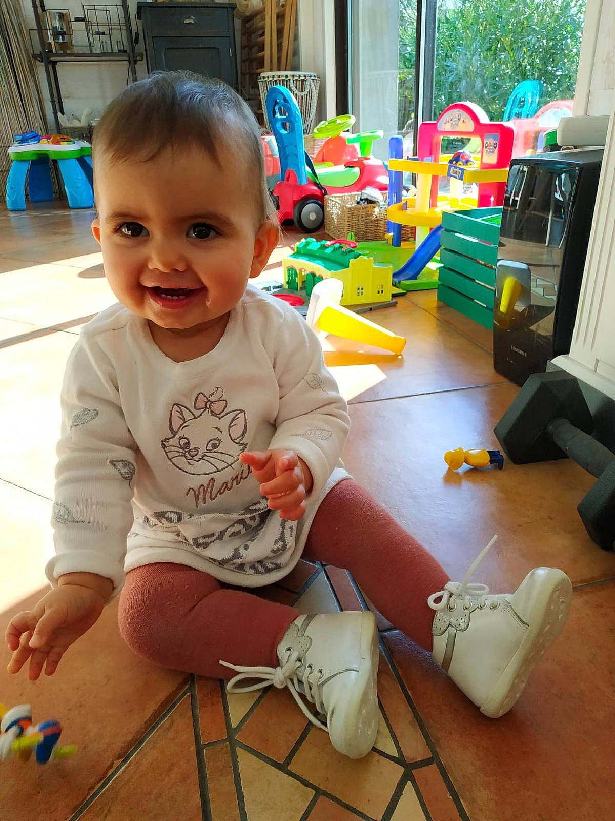 Elyana participe au concours pour gagner de l'argent avec cette photo : baby, baby_toddler_clothing, child, electronic_device, eye, floor, flooring, fun, hairstyle, happy, head, human_body, leg, person, skin, smile, snapshot, standing, toddler, toy