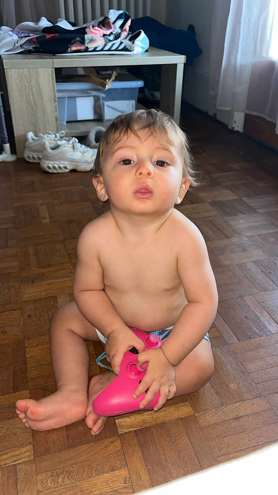 Hadriel a rejoint le concours — aidez-le/la à gagner de superbes lots ! toddler, child, floor, wooden_floor, controller, pink_controller, barefoot, indoor, home, table, shoes, curtains, clothing, person, sitting, skin, hair, expression, toy, casual
