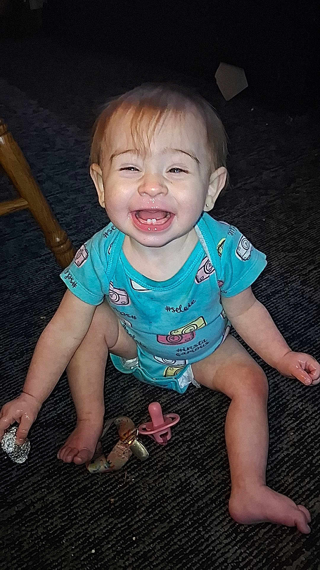 Ava is registered to the contest to win money with this photo: baby, child, smiling, onesie, blue_clothing, pacifier, carpet, indoor, happy, sitting, toy, face, hand, foot, hair, eating, cute, infant, playful, expression