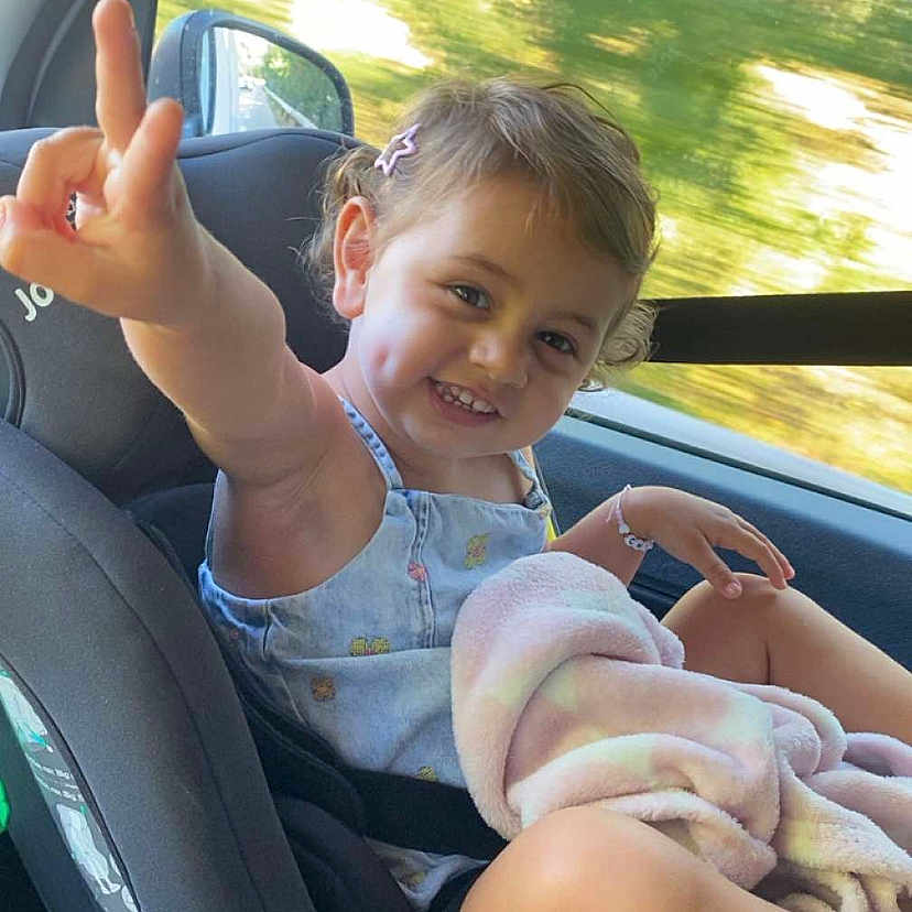 Chiara a rejoint le concours — aidez-le/la à gagner de superbes lots ! blanket, car_interior, car_seat, child, curly_hair, dimples, gesture, hair_clip, happy, outdoor_light, playful, portrait, seatbelt, sitting, smile, summer_clothing, toddler, travel, window, young_child