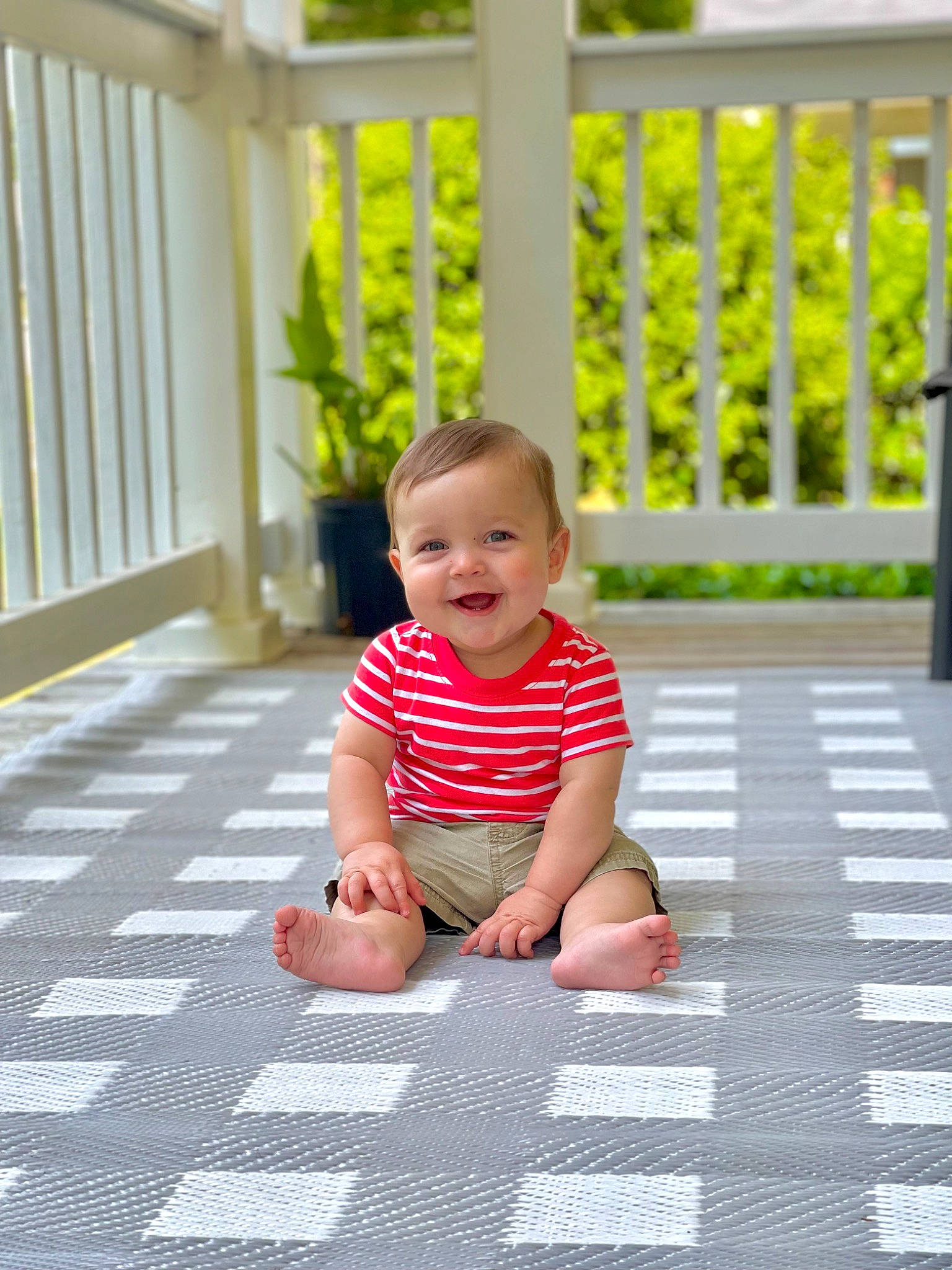 Finnley is registered to the contest to win money with this photo: baby, baby_toddler_clothing, child, crawling, fence, floor, flooring, fun, grass, happy, hardwood, joy, mammal, pattern, person, plant, road_surface, sitting, smile, t_shirt