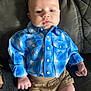 baby, infant, blue_shirt, plaid, shorts, couch, gray, person, child, face, skin, hand, leg, seated, indoors, clothing, casual, young, expression, portrait
