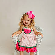 Brynlee is registered to the contest to win money with this photo: child, girl, curly_hair, pink_bow, watermelon_dress, white_chair, sitting, smiling, barefoot, studio, portrait, cute, happy, fashion, colorful_clothing, young_child, indoor, light_background, playful, innocence