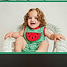Raylynn joined the competition — help win amazing prizes! toddler, child, curly_hair, smiling, green_striped_clothing, watermelon_design, white_wicker_chair, sitting, happy, indoor, cute, portrait, baby, person, playful, young_child, comfortable, bright, casual, fun