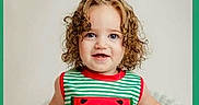 Raylynn joined the competition — help win amazing prizes! blue_eyes, casual_clothing, child, curly_hair, cute, fashion, framed_photo, green_border, happy, indoor, person, portrait, smiling, standing, striped_shirt, tank_top, toddler, watermelon_applique, white_wicker_chair, young_child