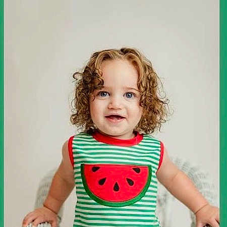 Raylynn joined the competition — help win amazing prizes! toddler, child, curly_hair, blue_eyes, striped_shirt, watermelon_applique, tank_top, white_wicker_chair, indoor, portrait, smiling, happy, cute, person, young_child, standing, framed_photo, green_border, fashion, casual_clothing