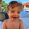 toddler, child, smiling, wet_hair, outdoor, poolside, blue_sky, sunny, happy, face, skin, eyes, mouth, teeth, snack, wrapper, background, red_building, green_chair, furniture