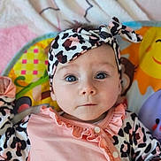 Lola participe au concours pour gagner de l'argent avec cette photo : baby, infant, headband, blue_eyes, pink_clothing, patterned_clothing, play_mat, colorful_background, cute, portrait, child, young, indoors, soft_lighting, curious_expression, lying_down, animal_print, ruffles, buttoned_clothing, face
