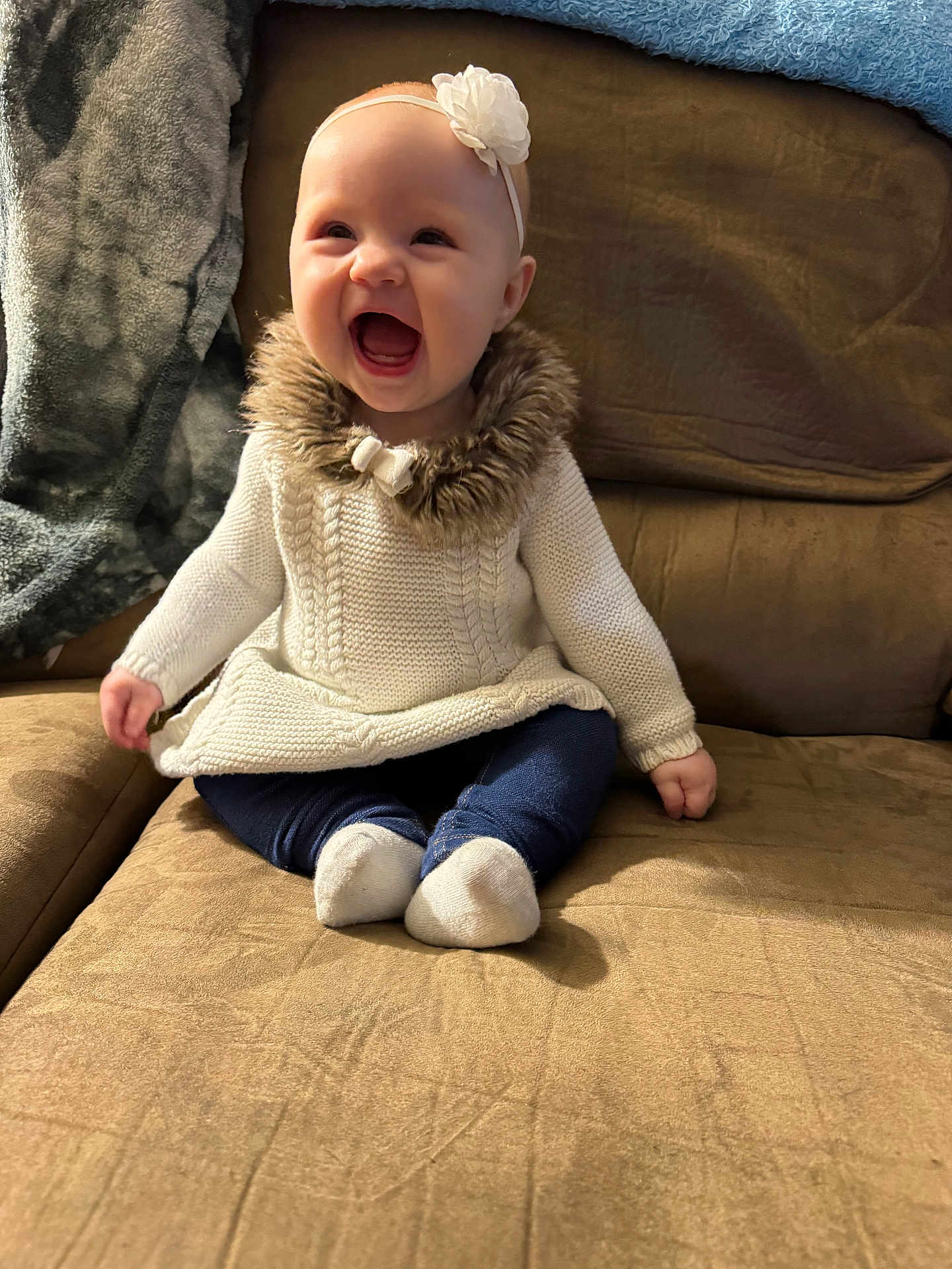 Brooklin joined the competition — help win amazing prizes! baby, smiling, sitting, couch, white_sweater, fur_collar, headband, flower, blue_pants, white_socks, indoor, cozy, happy, child, infant, cute, portrait, soft_texture, warm_lighting, furniture