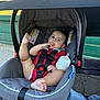 Blake is registered to the contest to win money with this photo: baby, stroller, car_seat, bottle, infant, child, red_clothing, outdoor, fence, chain_link_fence, seatbelt, canopy, foot, hand, face, person, blanket, fabric, toy, playground