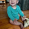toddler, child, baby, floor, wooden_floor, toy, toy_horse, onesie, clothing, living_room, couch, table, furniture, happy, smiling, sitting, indoor, person, skin, hand