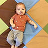 baby, child, infant, colorful_mat, playmat, cactus_shirt, orange_shirt, gray_pants, barefoot, lying_down, indoor, floor_mat, cute, smiling, young_child, one_child, baby_face, playtime, happy, casual_clothing