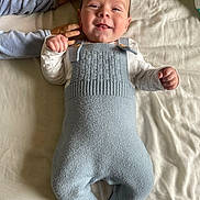 Hugo a rejoint le concours — aidez-le/la à gagner de superbes lots ! baby, child, smile, knitted_overalls, blue_clothing, white_shirt, hand, blanket, bed, sibling, cute, infant, happy, lying_down, face, person, soft_texture, cozy, indoor, young_child
