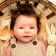 Harper a rejoint le concours — aidez-le/la à gagner de superbes lots ! baby, infant, knitted_blanket, wooden_basket, crocheted_toy, plush_bunny, face, blue_eyes, button_overalls, portrait, cute, soft_lighting, indoors, cozy, newborn, child, smiling, knitwear, warm_colors, sleepy