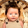 baby, infant, knitted_blanket, wooden_basket, crocheted_toy, plush_bunny, face, blue_eyes, button_overalls, portrait, cute, soft_lighting, indoors, cozy, newborn, child, smiling, knitwear, warm_colors, sleepy