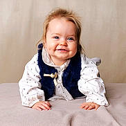 Lina participe au concours pour gagner de l'argent avec cette photo : baby, child, smiling, blue_eyes, dimples, white_clothing, navy_vest, blanket, soft_texture, portrait, cute, happy, infant, crawling, indoor, face, hands, light_background, young_child, studio_photo