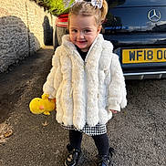 Milah-Bleu is registered to the contest to win money with this photo: black_car, black_shoes, car, child, fur_coat, hair_bows, license_plate, mercedes, outdoor, pavement, plush_toy, shadow, skirt, smile, stone_wall, sunny, tights, toddler, white_coat, yellow_duck